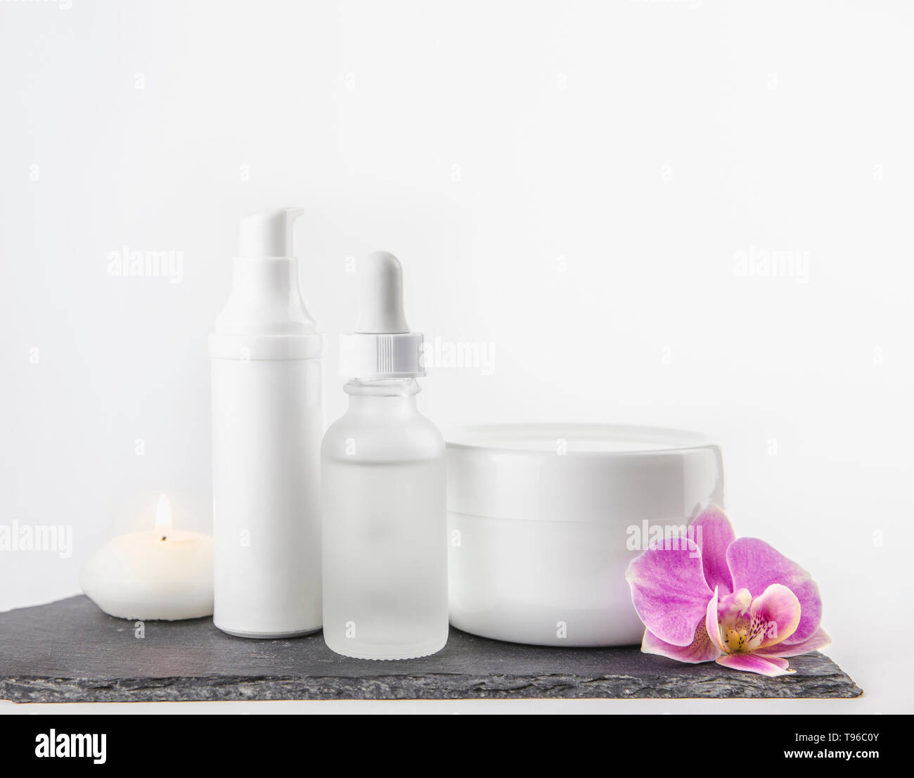 La forme et la taille du matériel différent de produit cosmétique de la crème, des contenants d'huile sur fond blanc debout sur socle de pierre noire, rose orchid Blossom. Banque D'Images