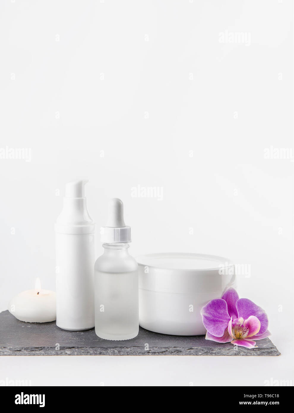 La forme et la taille du matériel différent de produit cosmétique de la crème, des contenants d'huile sur fond blanc debout sur socle de pierre noire, rose orchid Blossom. Banque D'Images