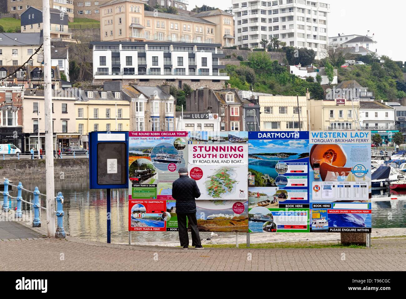 Vue arrière d'un homme âgé à la couleur à un avis du conseil en publicité voyages touristes Torquay sur différents types de transport, Devon, Angleterre Banque D'Images