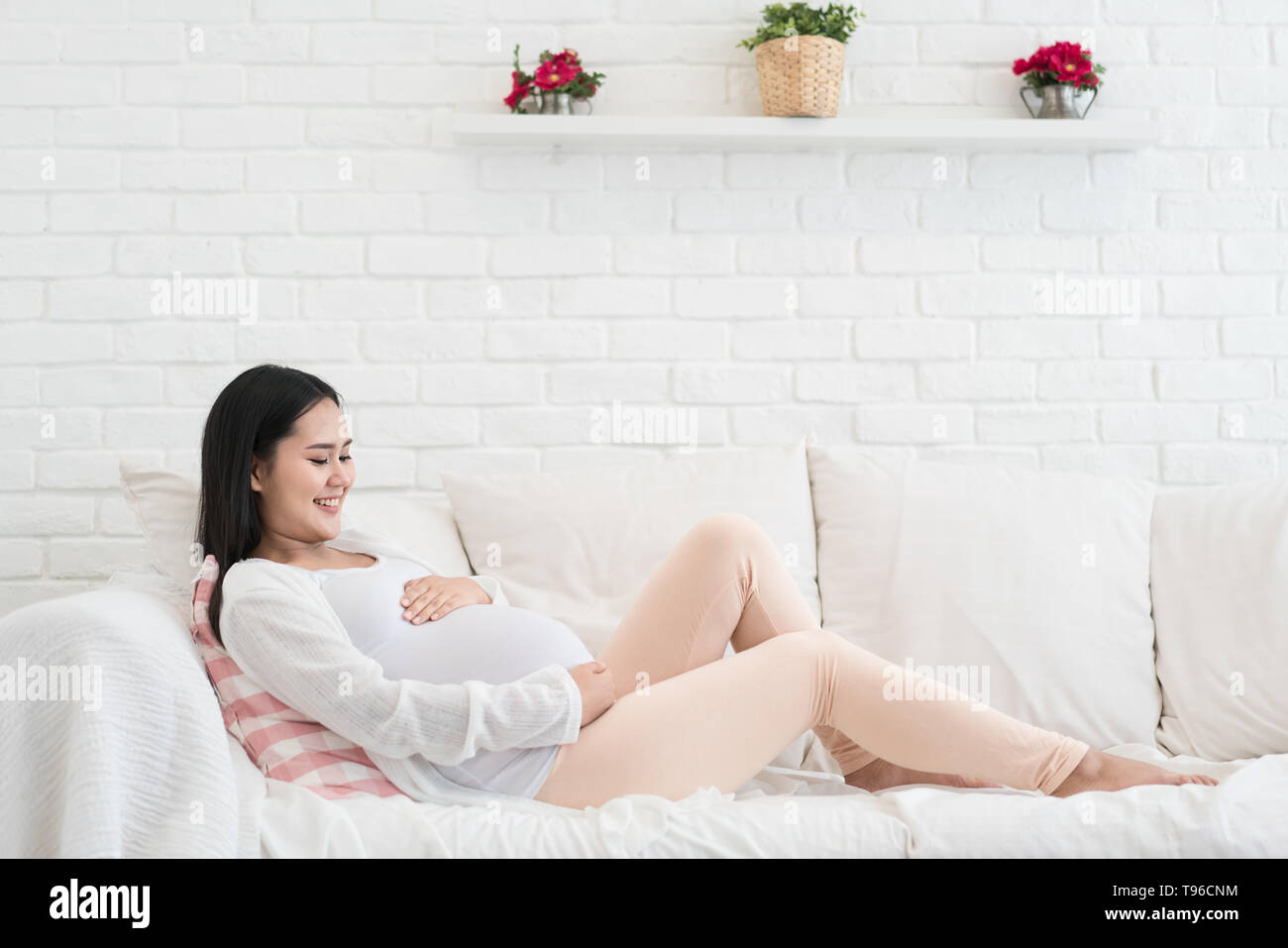 La grossesse, la maternité, les gens et l'attente concept - Close up of happy Asianpregnant femme avec gros ventre sur le canapé dans la salle de séjour à la maison. Banque D'Images