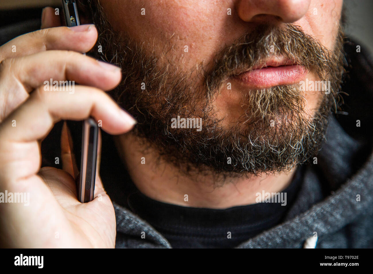 Portrait d'homme barbu en conversation sur téléphone intelligent, l'accent sur les lèvres, pas d'yeux, secret talk, criminel threating quelqu Banque D'Images