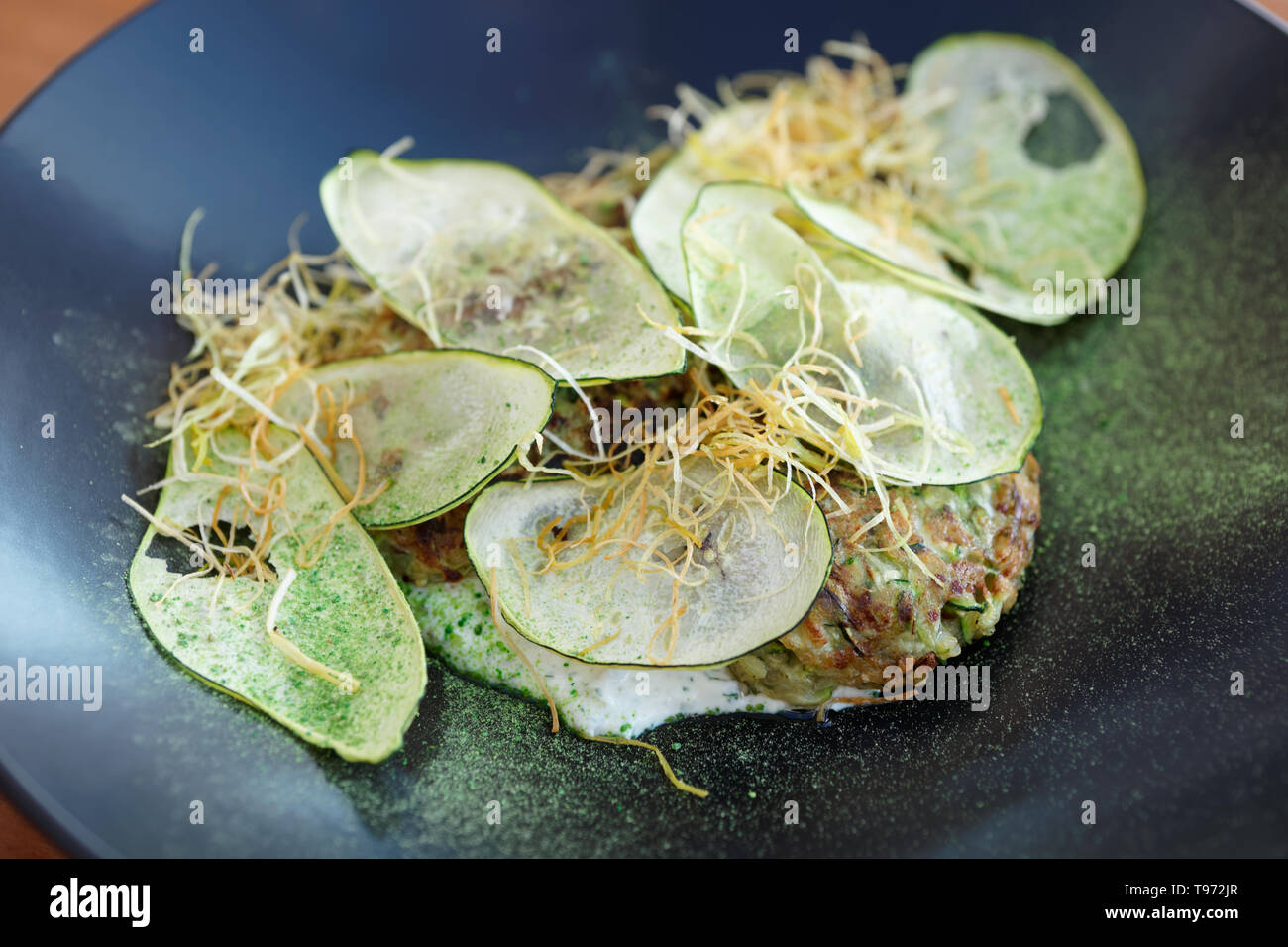 Apéritif végétarien gastronomique créative - beignet de courgettes avec les croustilles de légumes et l'oignon frit sur la plaque noire Banque D'Images