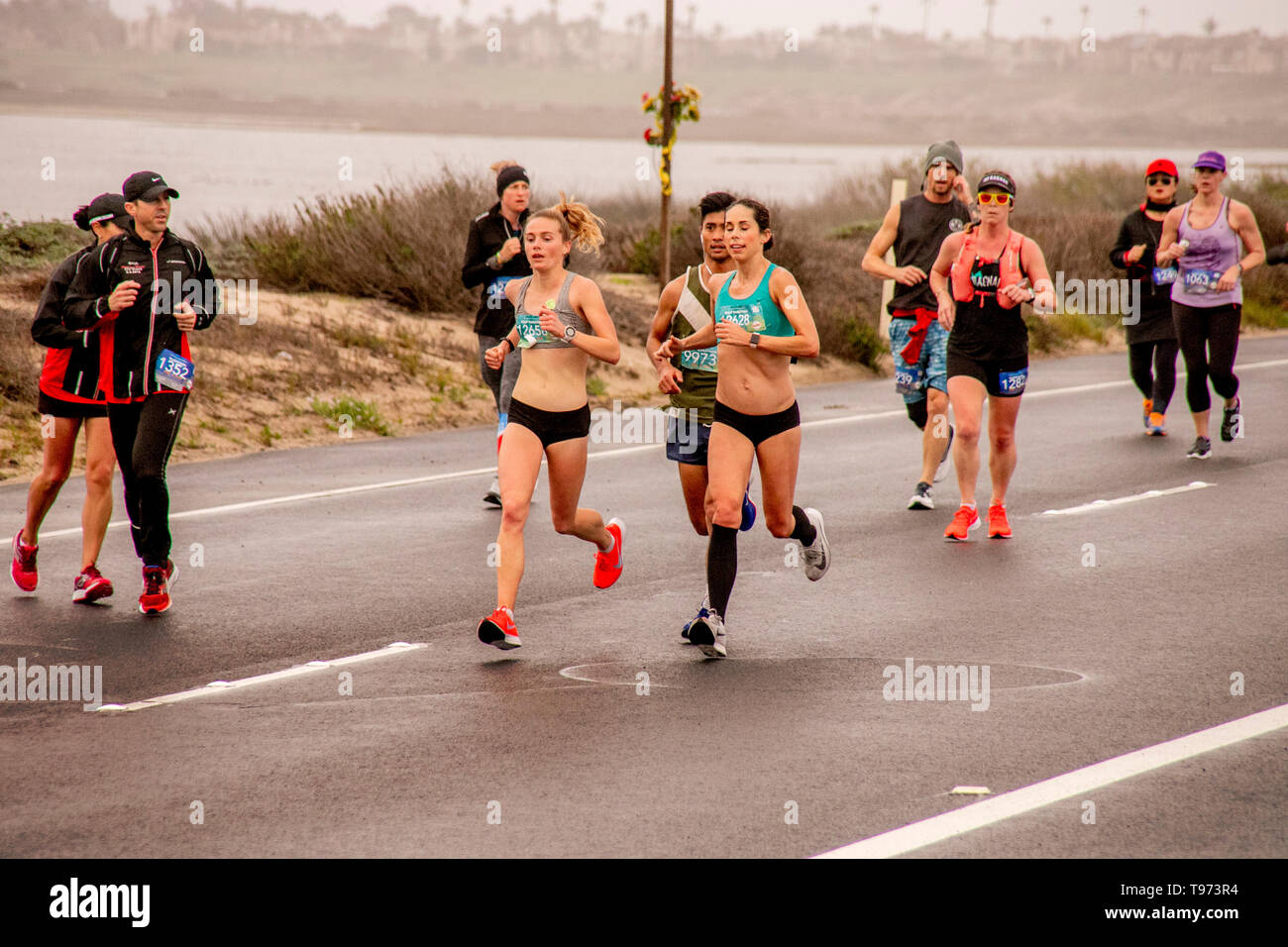 En tant que bénévoles par stand d'offrir de l'aide, femme demi-marathon d'investiture courir le long d'une route dans la région de Huntington Beach, CA. Banque D'Images