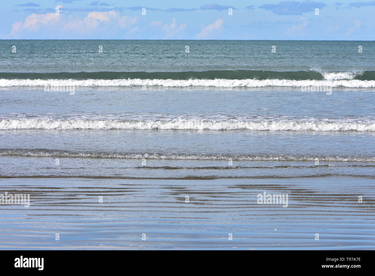 Des rangées de minuscules vagues de surf de matériel roulant à l'océan calme plage de sable plat. Banque D'Images