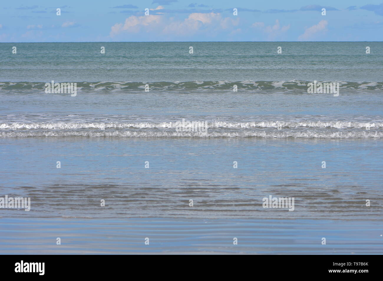 Des rangées de minuscules vagues surf venant de l'océan calme plat à plage de sable. Banque D'Images