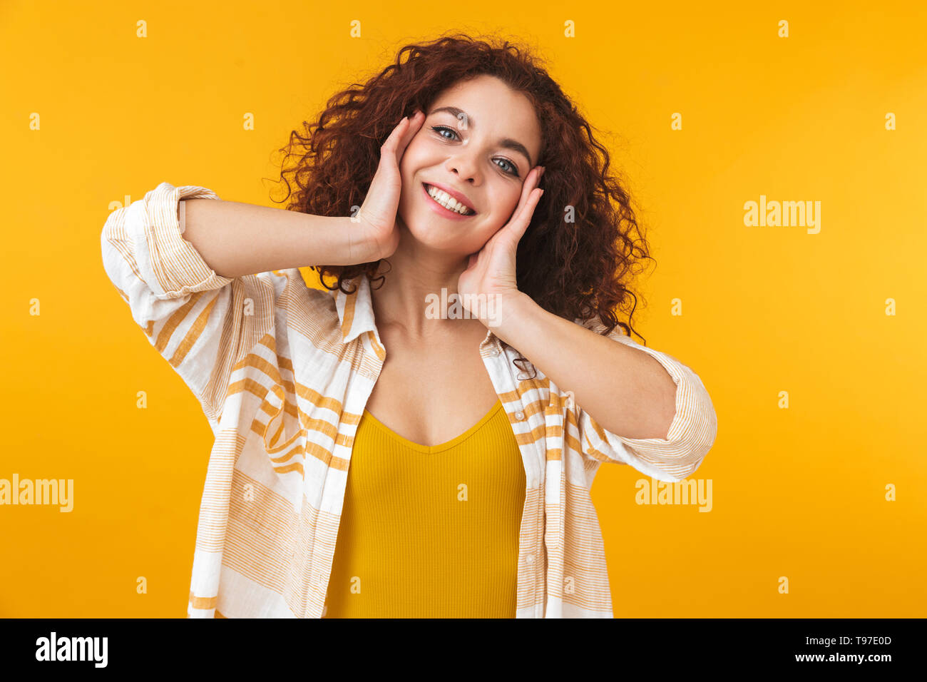 Image de belle femme 20s avec des cheveux bouclés standing and smiling, isolé sur fond jaune Banque D'Images