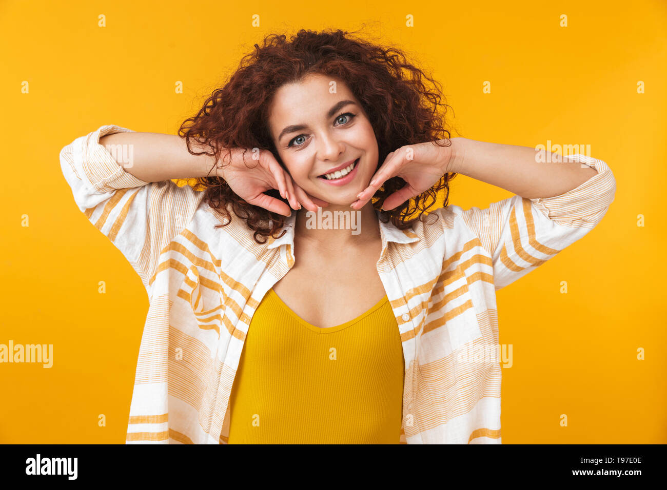 Image de femme readhead 20s avec des cheveux bouclés standing and smiling, isolé sur fond jaune Banque D'Images