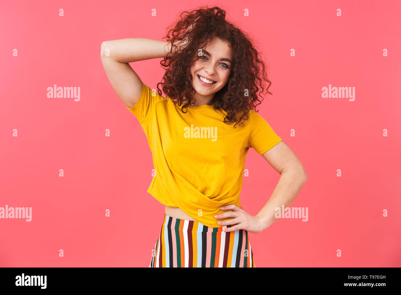 Photo de belle femme 20s avec des cheveux bouclés standing and smiling, isolé sur fond rose Banque D'Images