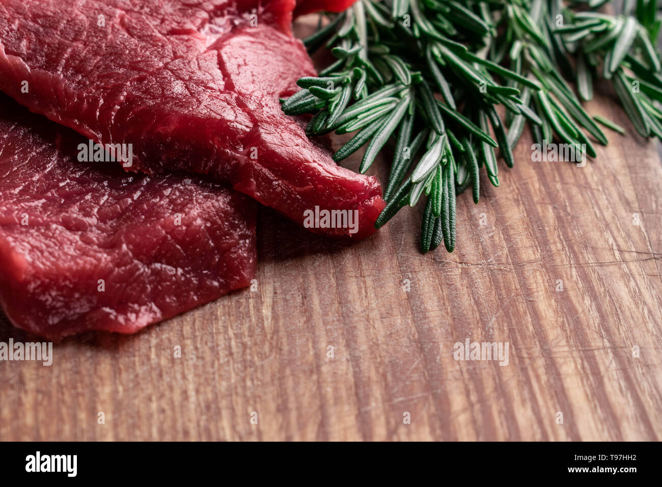 Deux morceaux de viande de boeuf avec des branches de romarin vert lumière se situent sur une planche en bois avec un espace vide pour le texte Banque D'Images