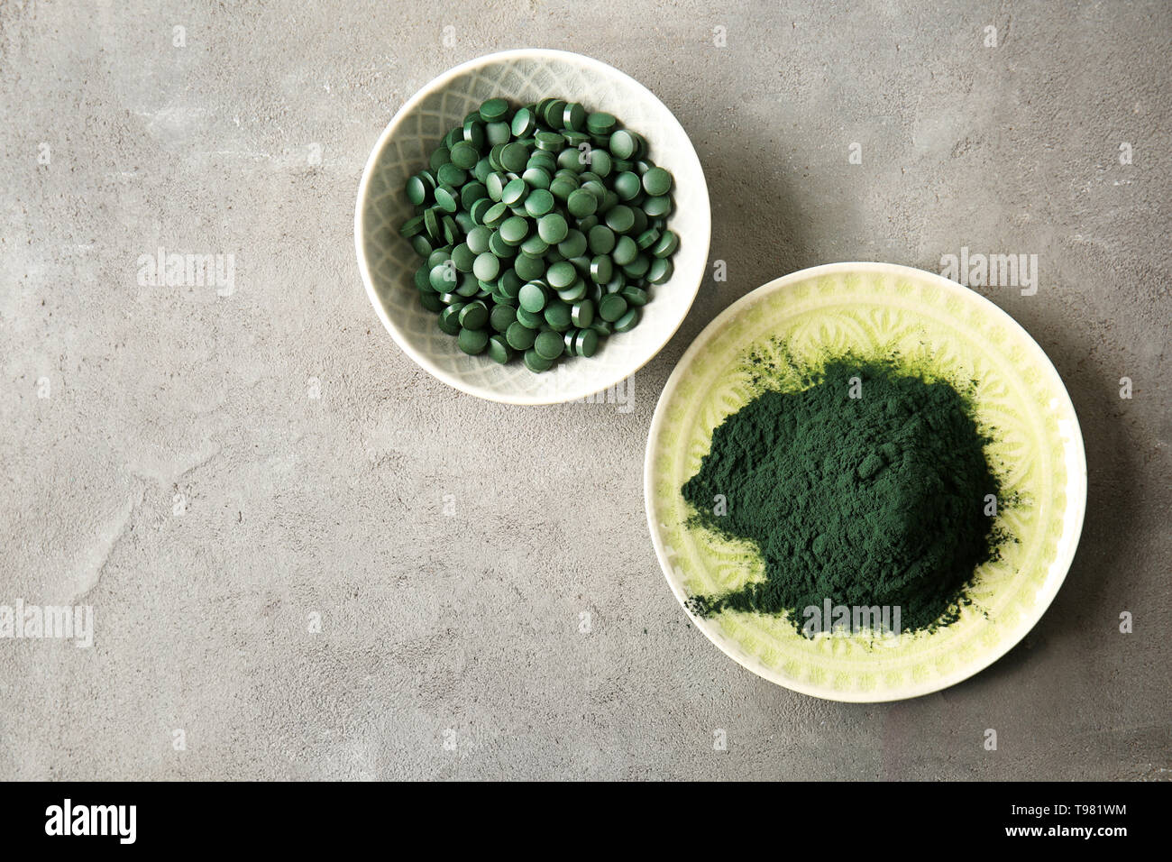 Les plaques avec la spiruline en comprimés et poudre sur table gris Banque D'Images