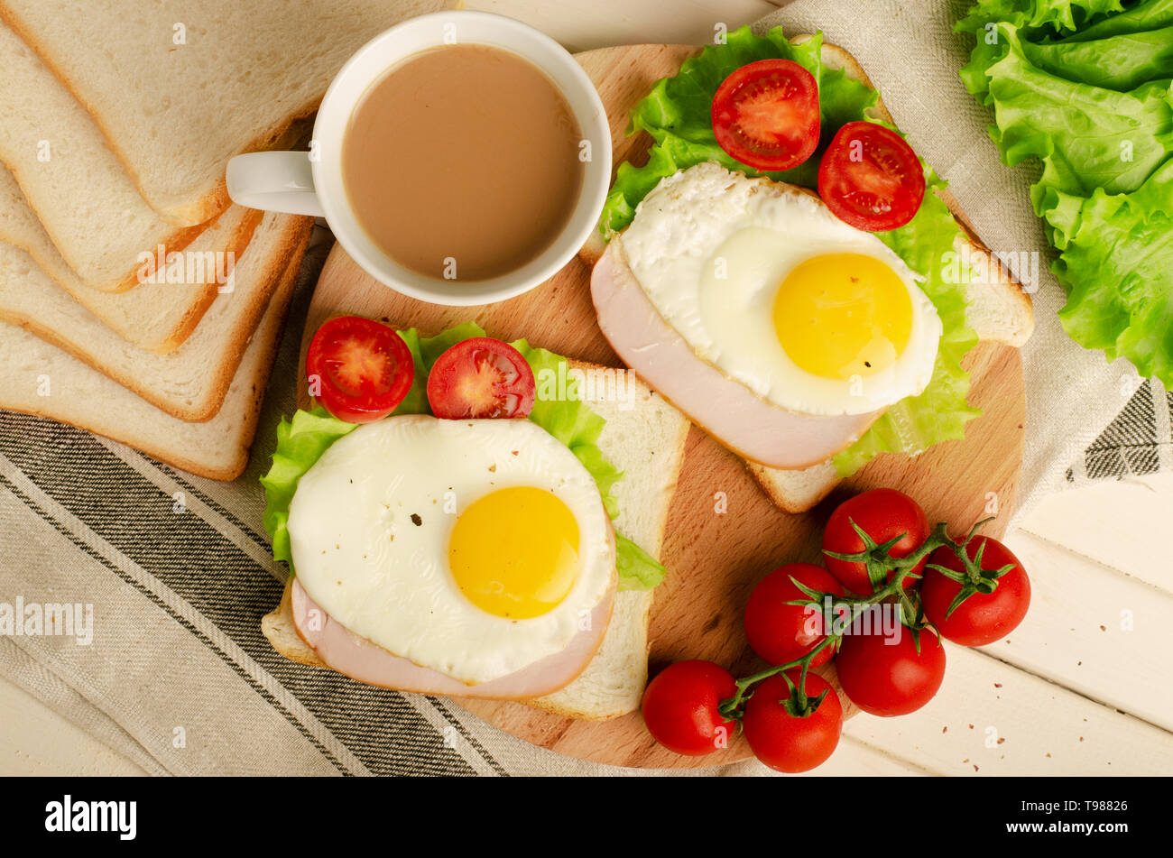 Sandwich au jambon avec des œufs brouillés, tomate, salade, petit-déjeuner sain et délicieux café sur fond de bois blanc Banque D'Images