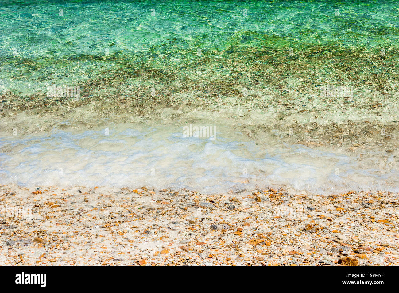 Vagues douces avec de la mousse d'eau sur les cailloux et plage de sable. Banque D'Images