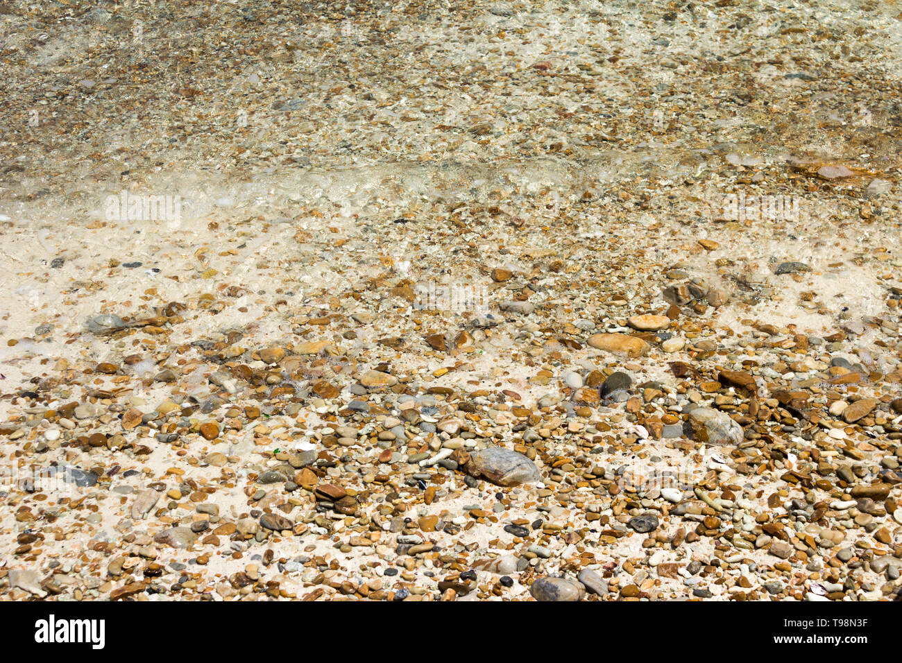 Vagues douces avec de la mousse d'eau sur les cailloux et plage de sable. Banque D'Images