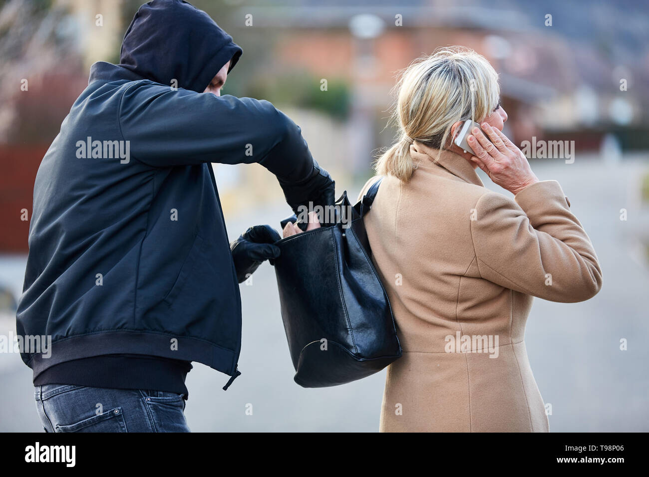 Voleur vole le portefeuille de son sac à main à une femme qui est au téléphone Banque D'Images