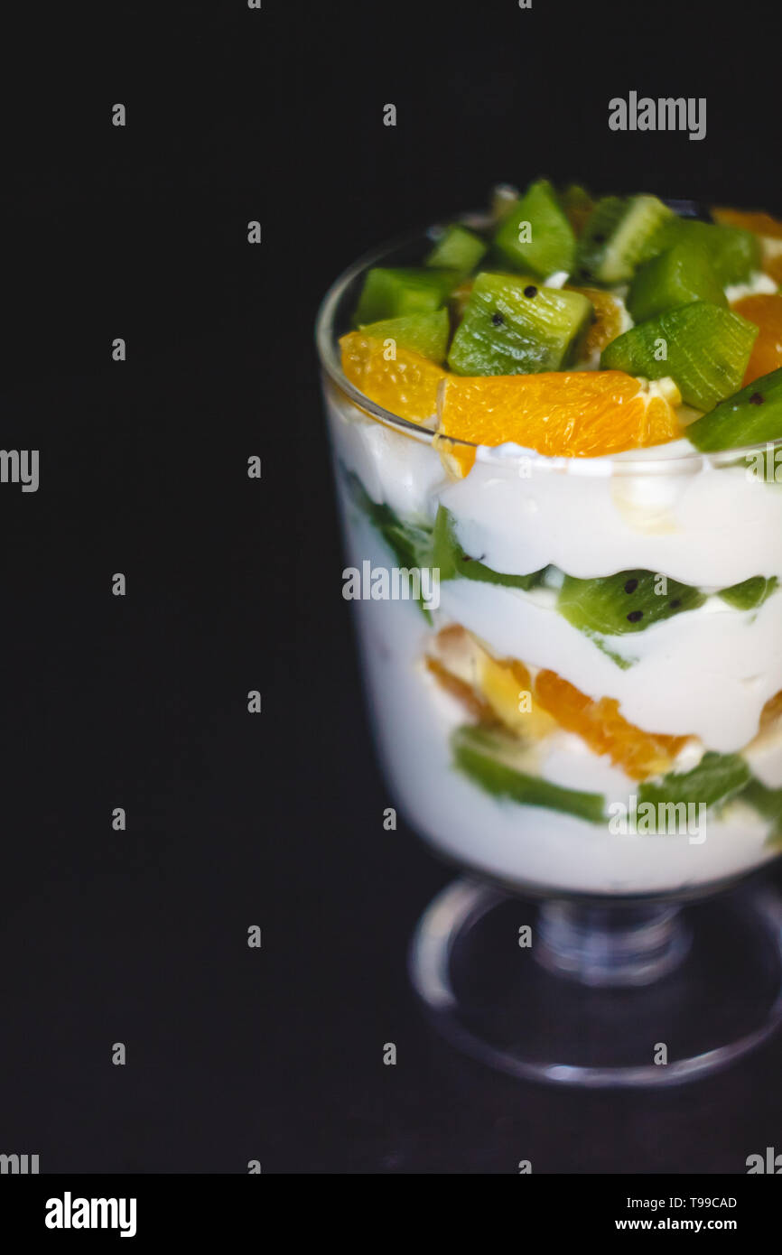 Dessert en couches dans un verre transparent, yaourt, orange, kiwi, noix sur un fond sombre. Le concept de la saine, bonne et simple des aliments sains Banque D'Images