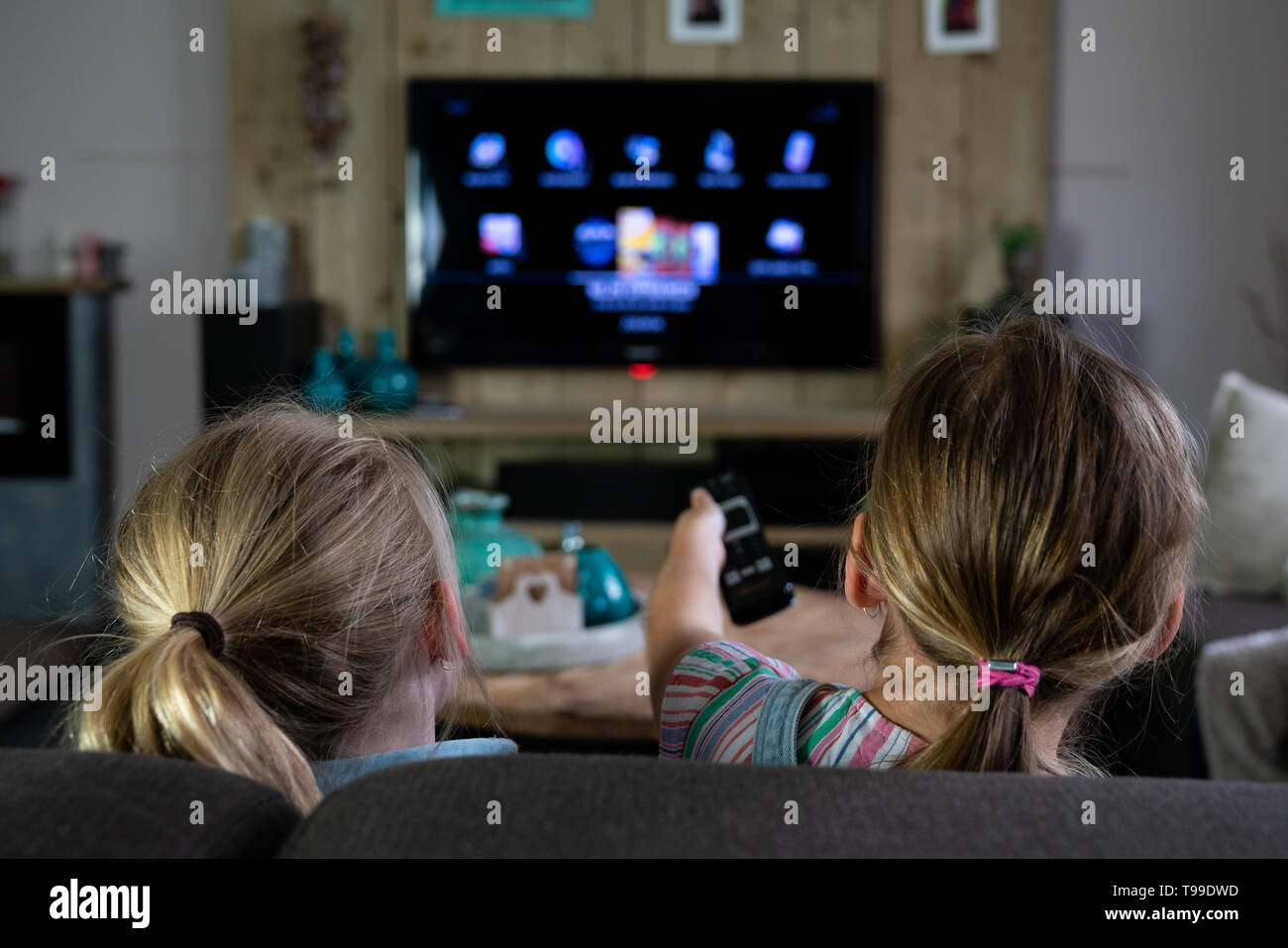 Vue arrière de deux enfants glissant à travers les applications sur une télévision intelligente. retour des enfants avec l'accent mis sur la télécommande. Le futurisme au quotidien Banque D'Images