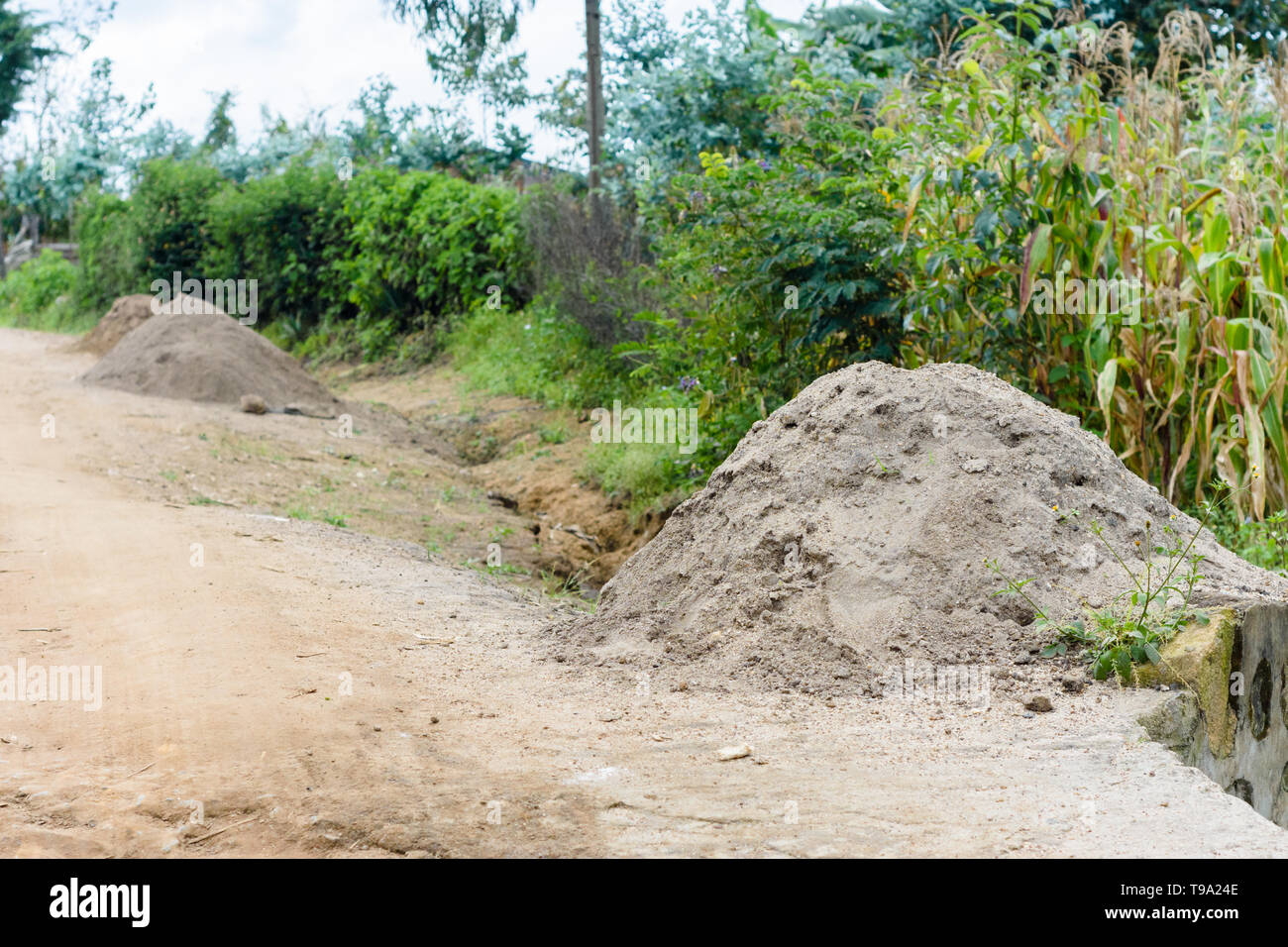 Le sable de construction creusée d'une rivière et entassé dans des piles pour la vente pour la construction sur le bord d'une route de terre dans un village du Malawi Banque D'Images