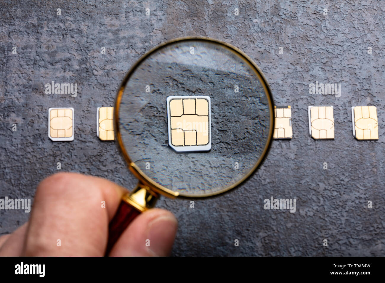 Person's Hand Holding Loupe sur Nano carte Sim sur fond rugueux Banque D'Images