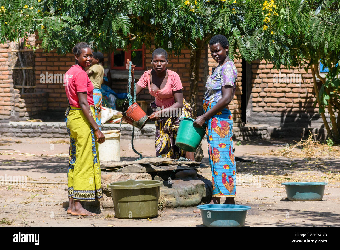 Les femmes du Malawi dans l'eau dessin soleil de midi à partir d'un puits dans un village à l'aide de seaux en plastique et corde Banque D'Images