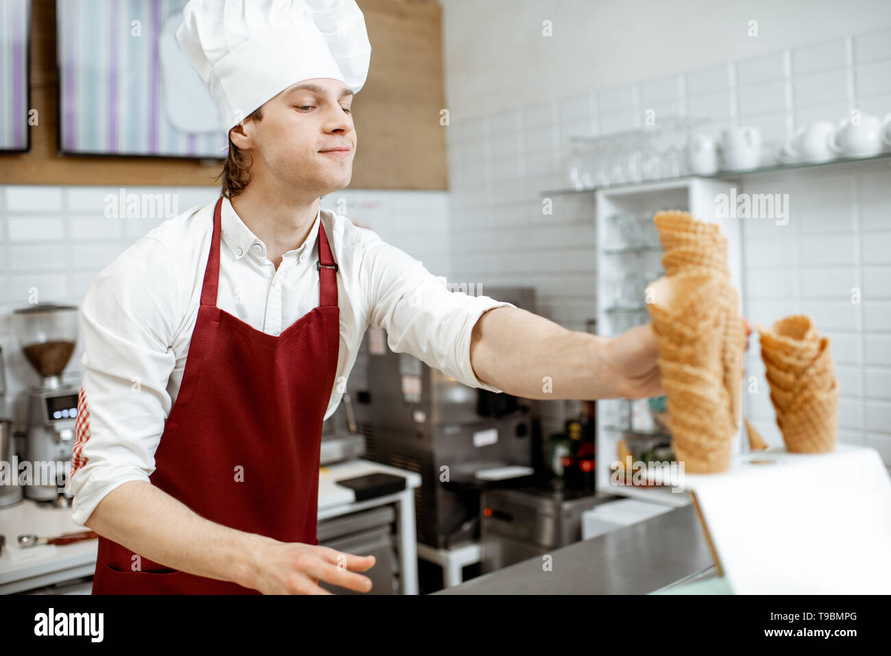 Beau vendeur en tablier et chapeau en tenant les cônes alvéolés tout en glace à la pâtisserie moderne Banque D'Images
