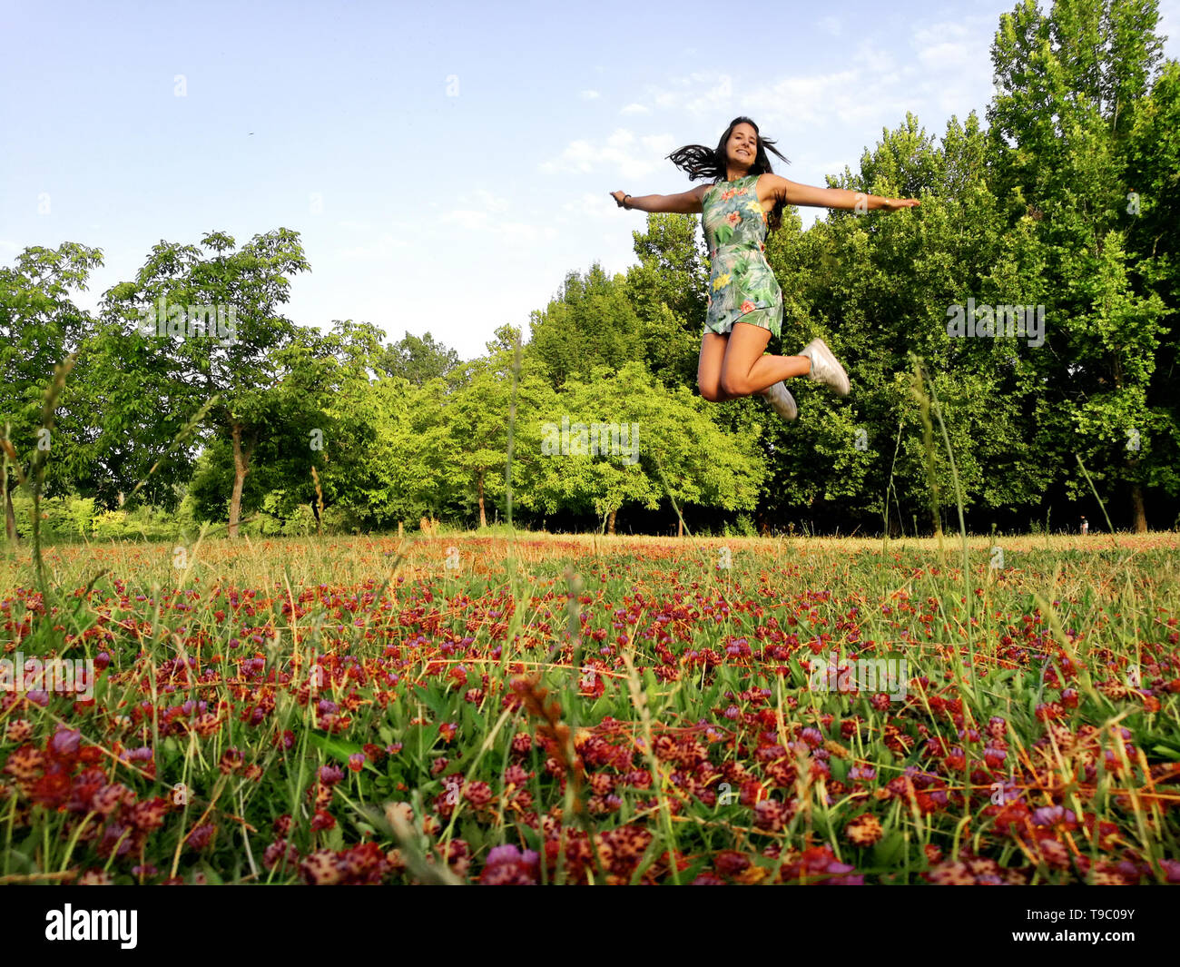 Happy young woman smiling femelle et le saut sur une pelouse avec des fleurs rouges dans un parc naturel. Girl in flower meadow, plaine de la beauté dans la nature, de l'Espagne. Banque D'Images