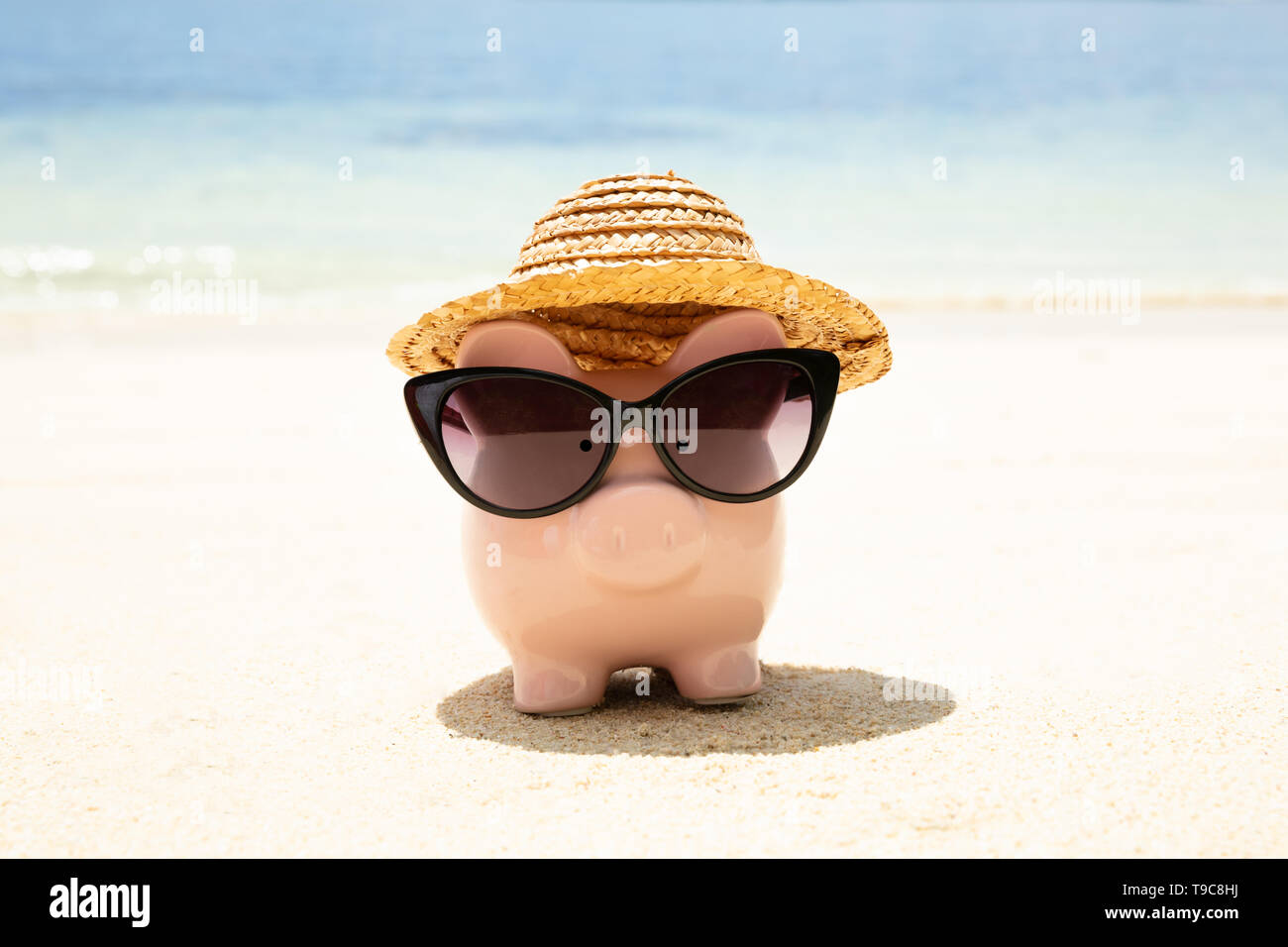 Pink Piggybank portant des lunettes noires sur le sable à la plage Banque D'Images