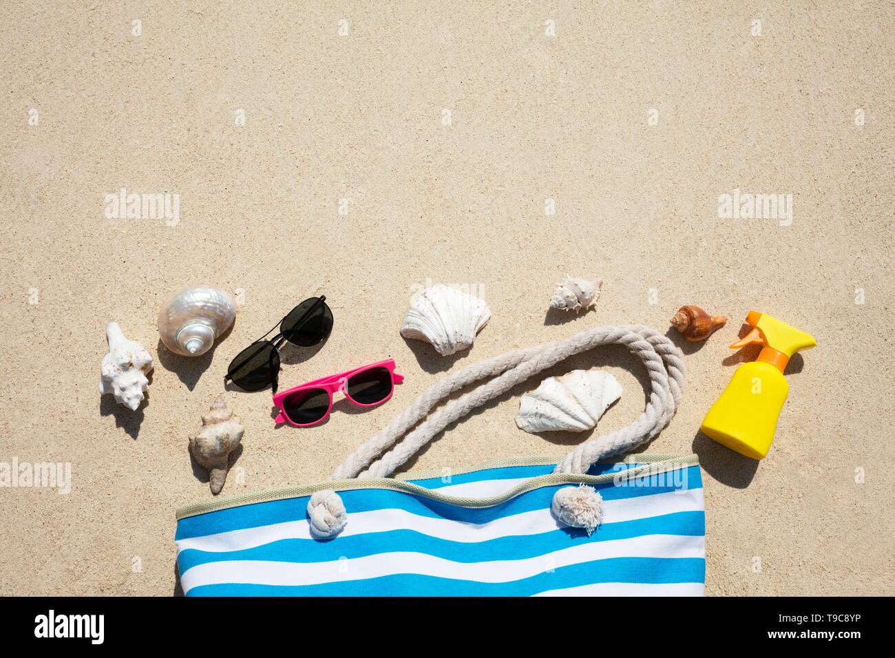 Les coquillages, lunettes de soleil, crème solaire et Bouteille Sac à Sand At Beach Banque D'Images