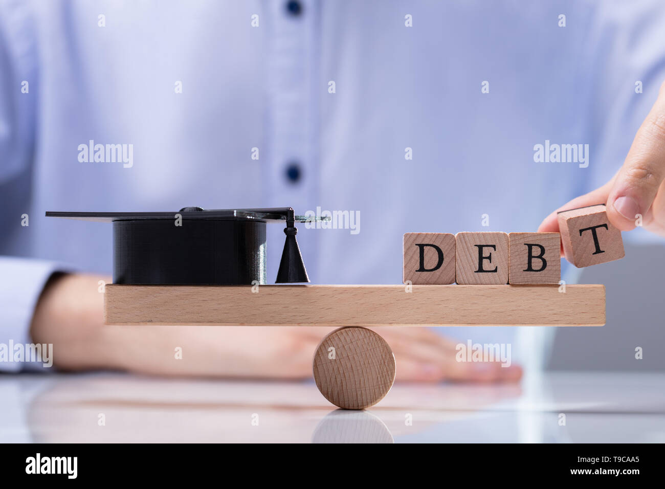 La main d'affaires Mettre mot sur la dette afin d'équilibrer la balançoire en bois noir Graduation Hat Banque D'Images