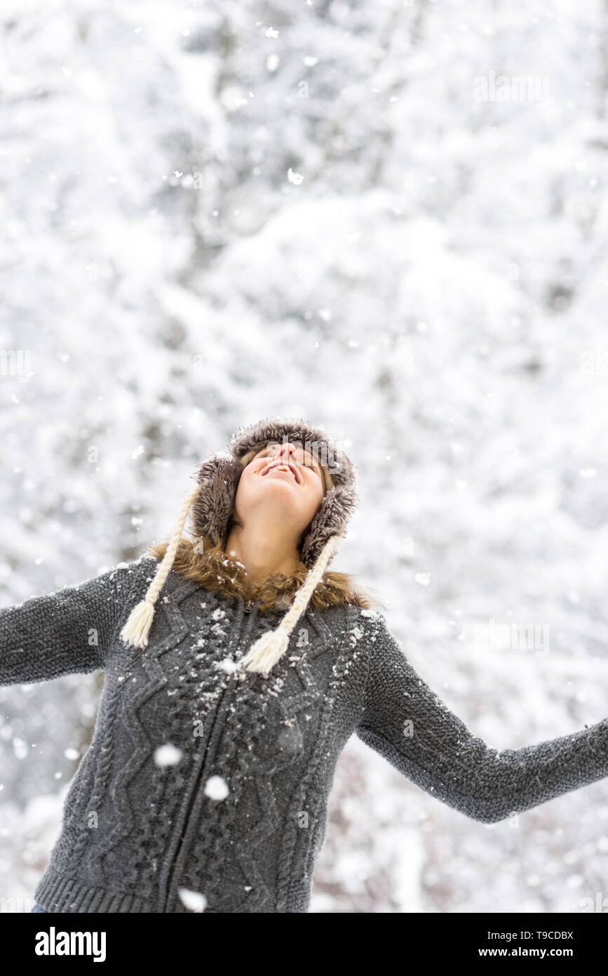 Femme joyeuse profiter de la neige de l'hiver jusqu'à la chute des flocons de neige dans le avec un sourire heureux et ses bras étendus, dans un contexte de snowy v Banque D'Images