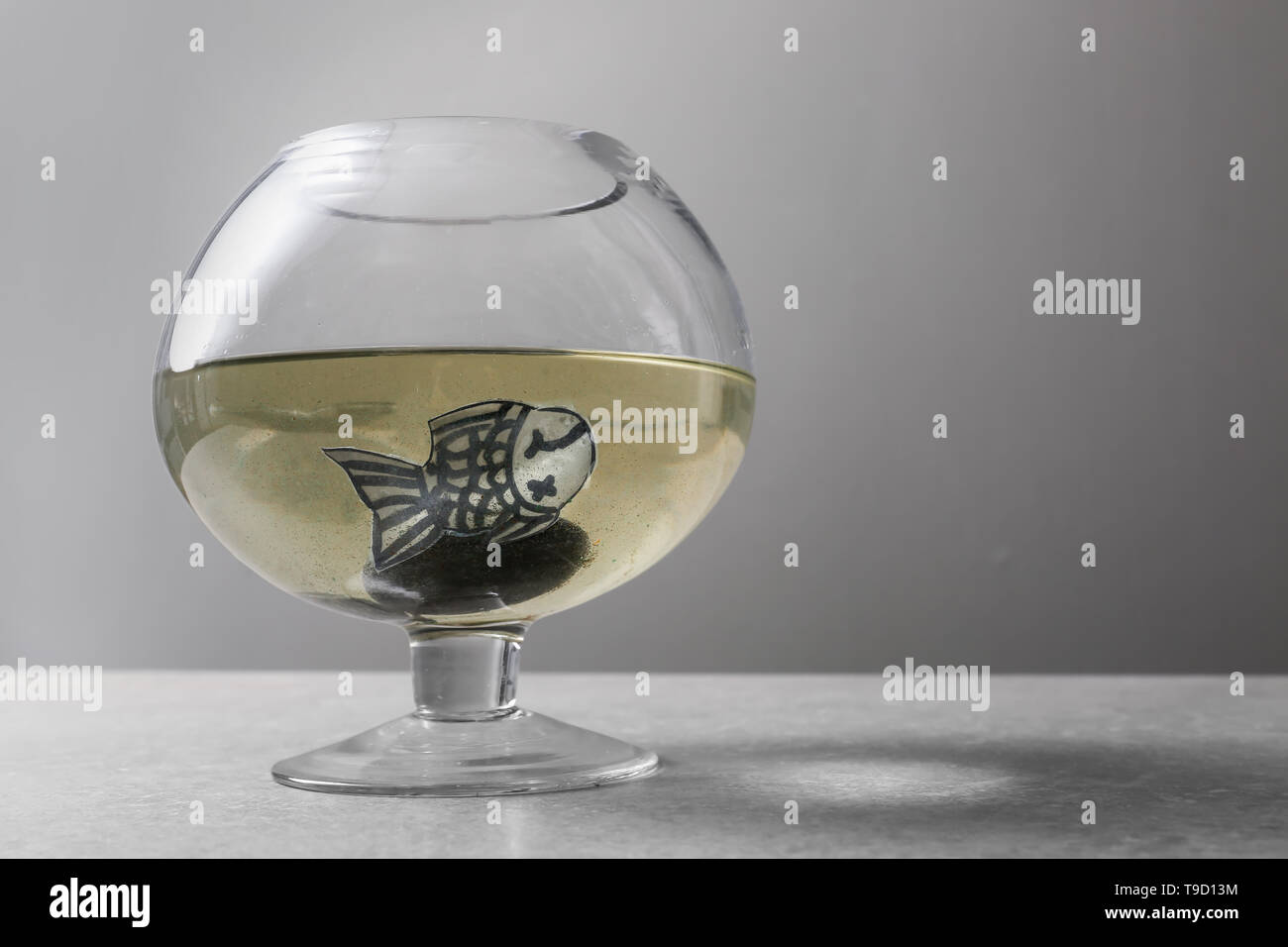 Aquarium avec l'eau sale et poisson de papier sur table gris Banque D'Images