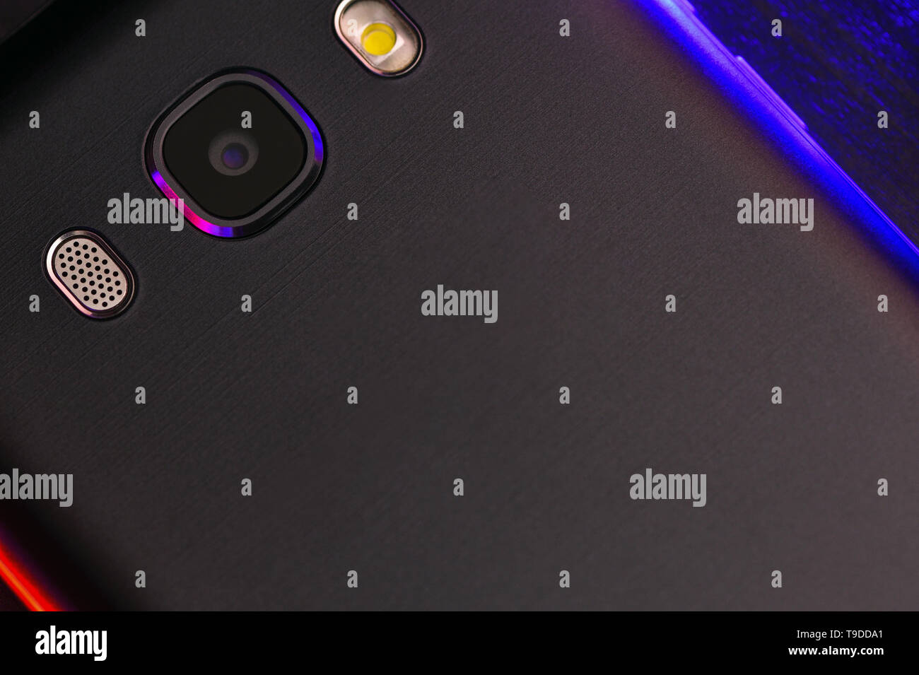 Un fragment de la téléphone cellulaire cas en noir avec rétro-éclairage bleu et rouge. Le téléphone se trouve sur la surface noire de l'appareil technologique avec un bleu Banque D'Images