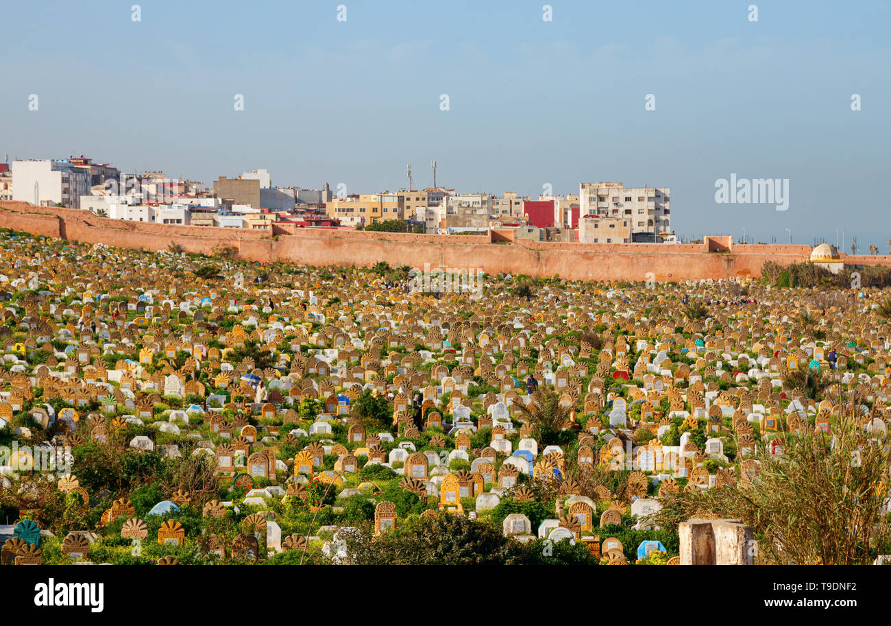 Cimetière avec des tombes et pierres tombales, recouvert d'herbe à la côte avec des bâtiments résidentiels à l'arrière-plan sur un après-midi ensoleillé. Rabat, Maroc. Banque D'Images