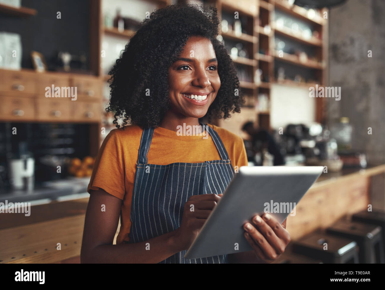 Jeune femme propriétaire debout dans cafe holding digital tablet Banque D'Images