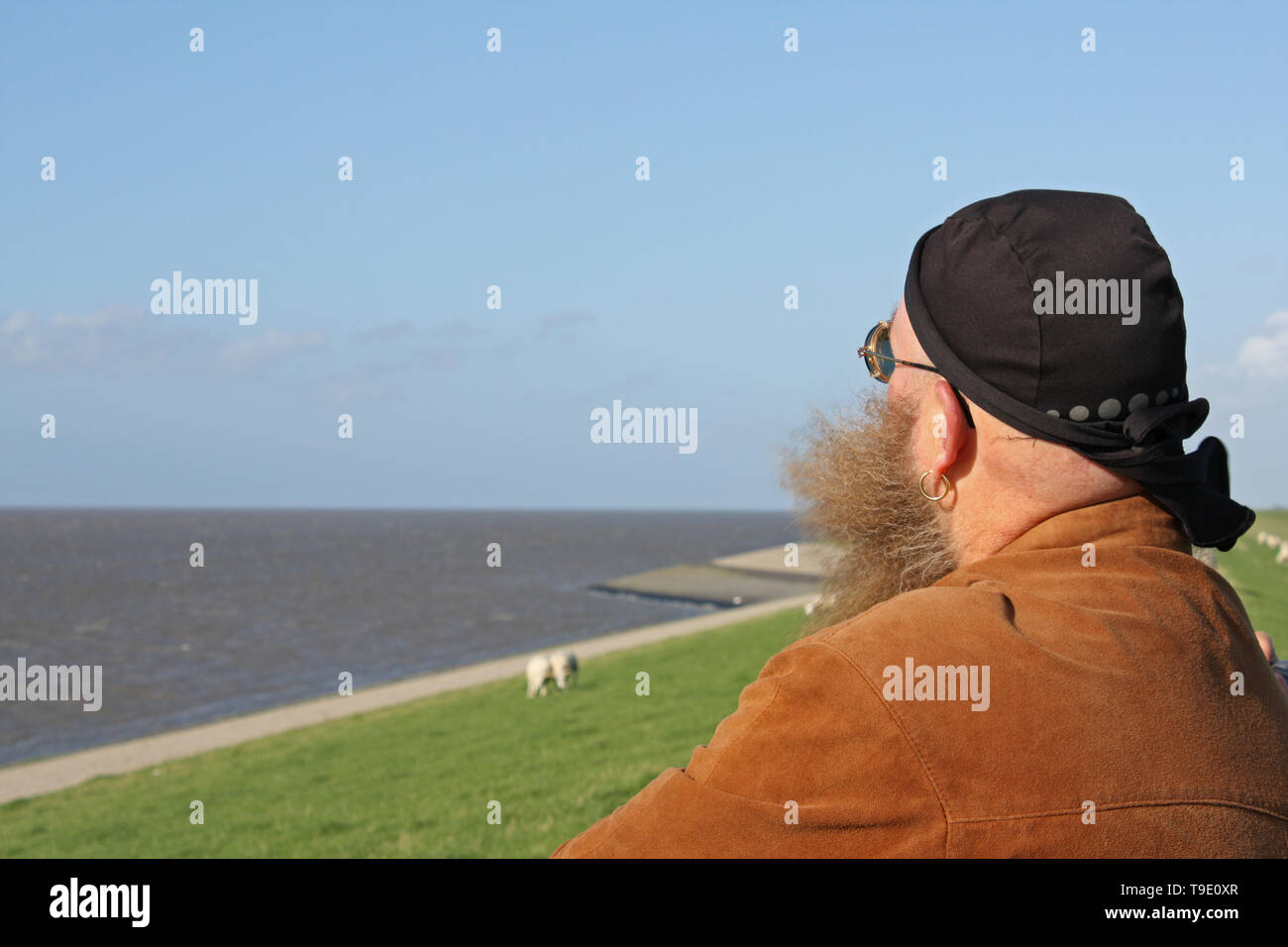 Mann mit langem Bart, der vom Wind verwirbelt wurde, steht Am Ufer des Meeres Banque D'Images