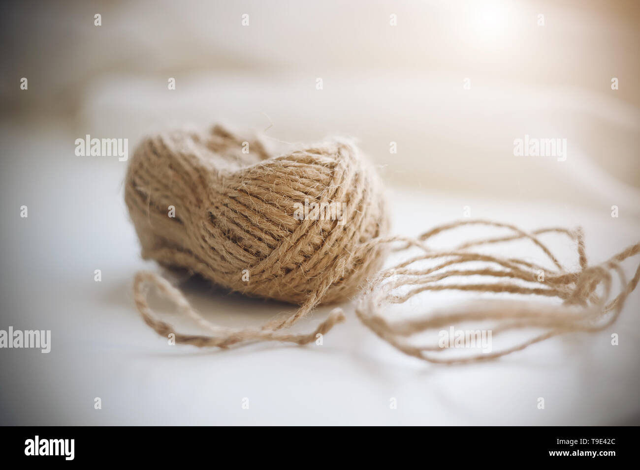 Une bobine de corde de chanvre grossier beige allongé sur un fond blanc et illuminé par la lumière du soleil. Banque D'Images