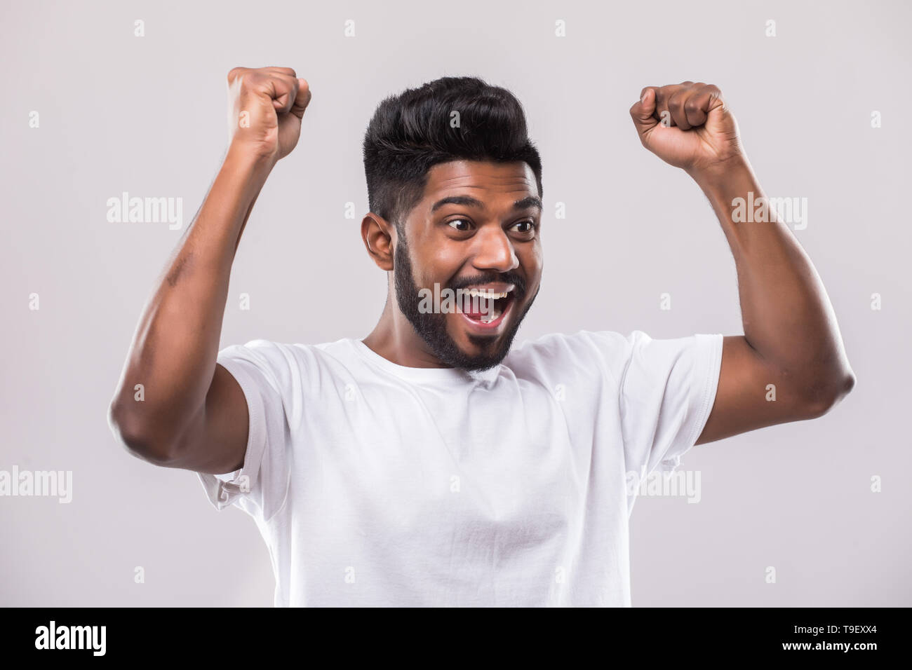 J'ai gagné. Happy young Indian man gesturing et smiling while standing against white background Banque D'Images