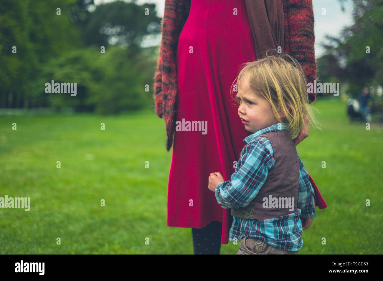 Un peu de tout-petit est accroché à sa mère sur une pelouse dans un parc de pays Banque D'Images