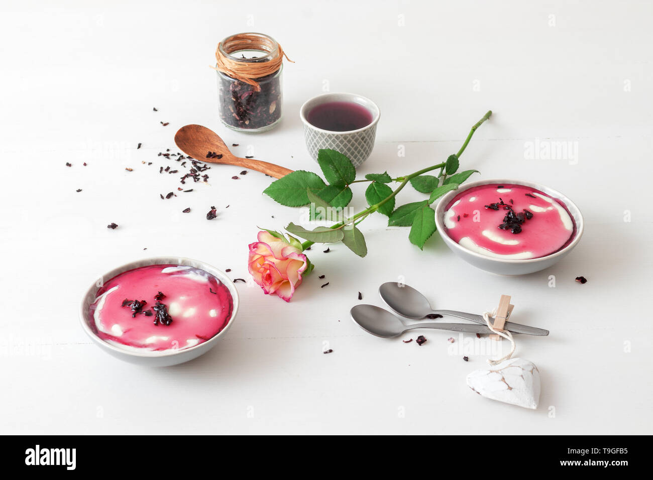 Dessert sucré traditionnel italien panna cotta aux sirop d'hibiscus. Table en bois blanc avec 2 bols de panna cotta, un petit bol de sirop d'hibiscus et ja Banque D'Images