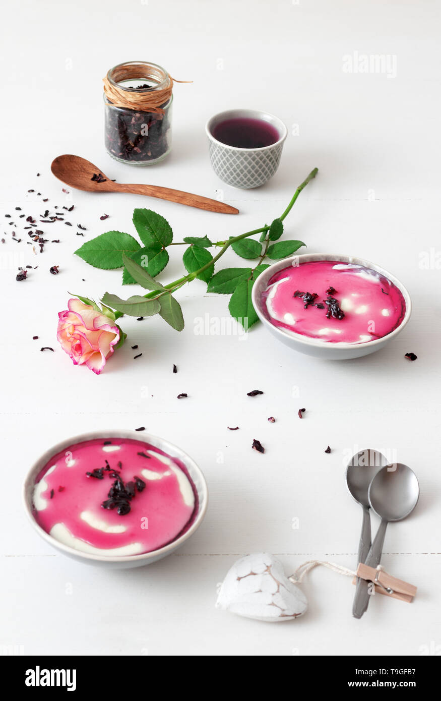Dessert sucré traditionnel italien panna cotta aux sirop d'hibiscus. Table en bois blanc avec 2 bols de panna cotta, un petit bol de sirop d'hibiscus et ja Banque D'Images