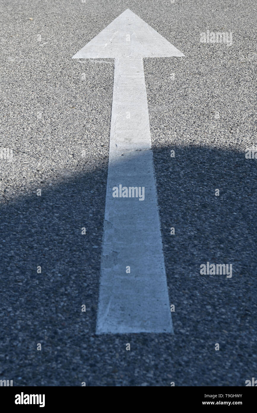 Signe d'asphalte : flèche blanche sur la texture du béton en sortie de l'ombre Banque D'Images