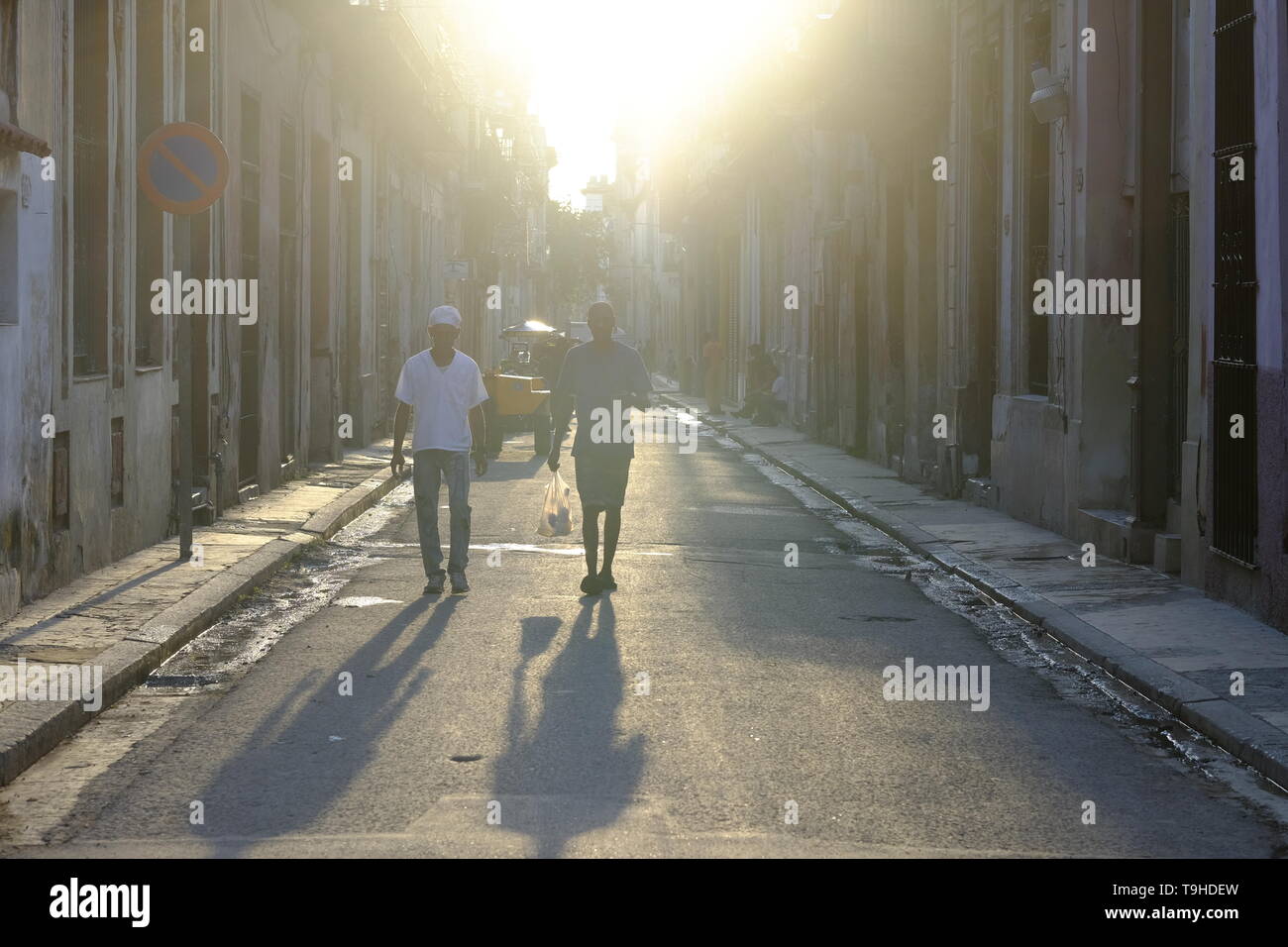 Le soleil du matin illumine deux personnes au travail à pied dans une rue de la Vieille Havane, Cuba Banque D'Images