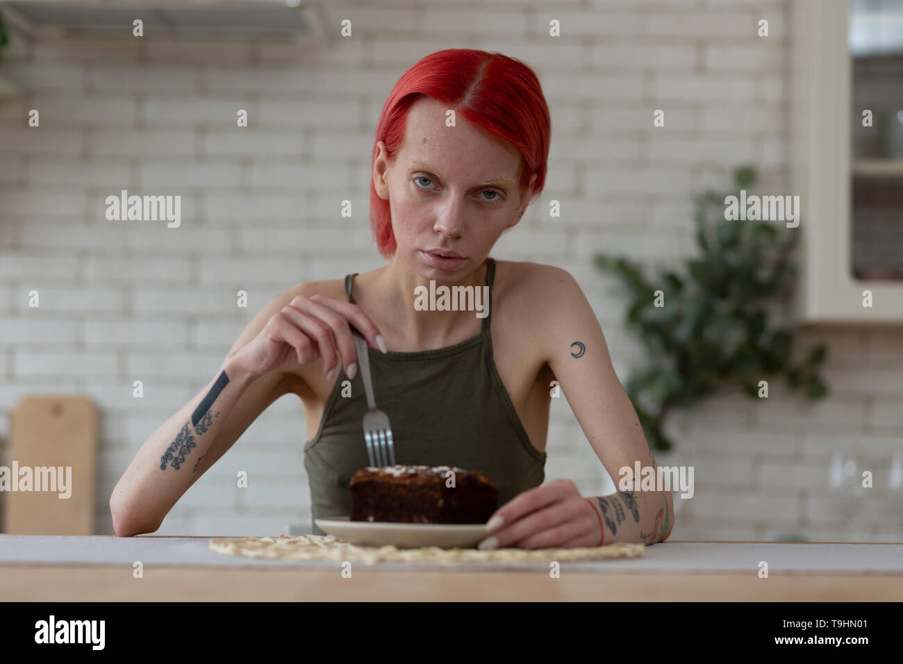 Femme anorexique avec des tatouages assis à la table avec un gâteau au chocolat Banque D'Images
