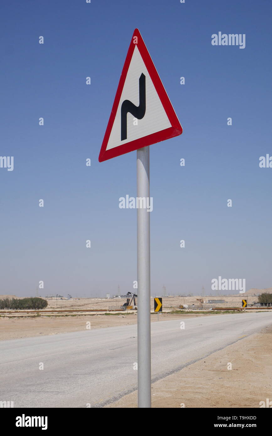Signe de route sur une route du désert se courbe montrant l'avant, Royaume de Bahreïn Banque D'Images
