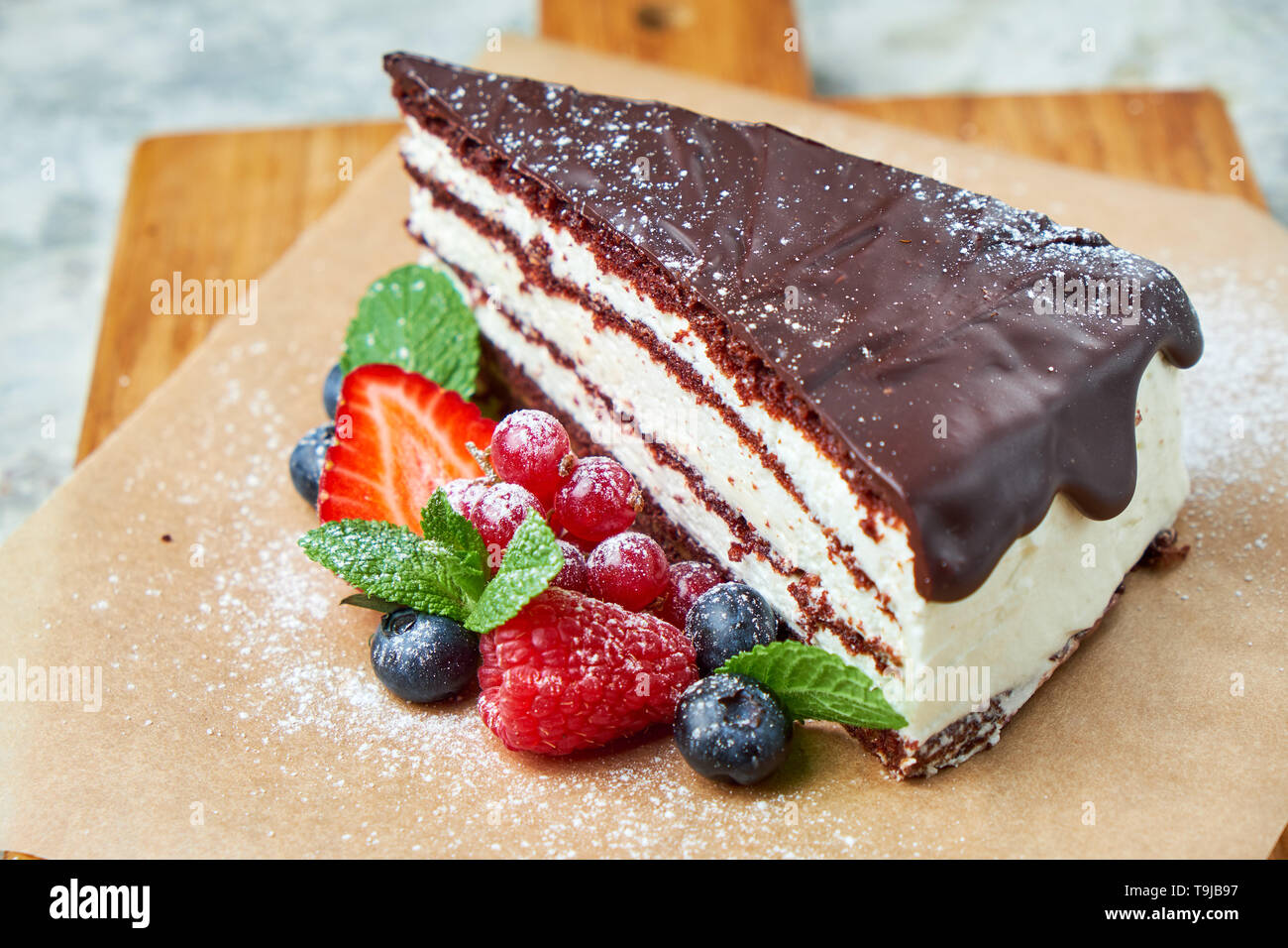 Une tranche de gâteau au chocolat décoré de petits fruits sur une planche de bois. Fond texturé gris. Beaux plats de service. Le Dessert. La chaîne alimentaire Banque D'Images