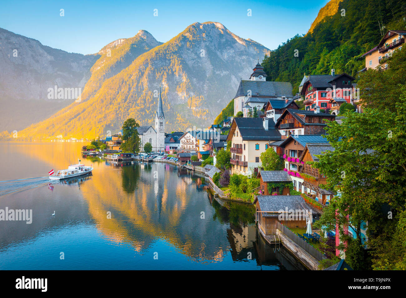 Vue de carte postale classique de la célèbre ville au bord du lac de Hallstatt dans les Alpes avec des passagers à bord d'un navire traditionnel au début de lumière du matin au lever du soleil, Autriche Banque D'Images