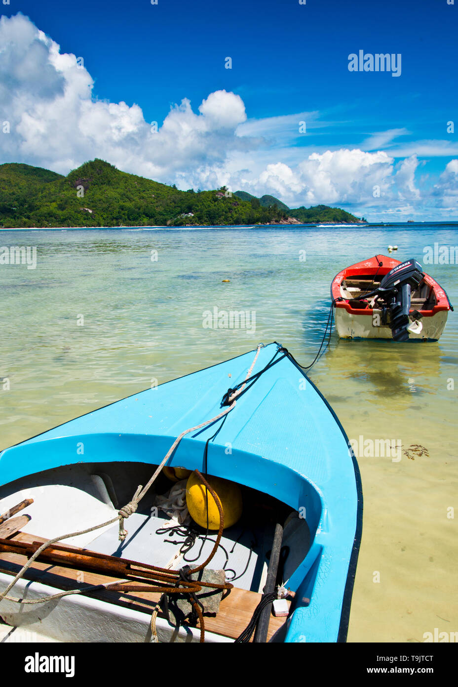 Petits bateaux de pêche colorés peints en bleu et rouge se sont rassemblés, avec ancrage de moteur extérieur dans la baie turquoise de l'océan, Seychelles, Banque D'Images