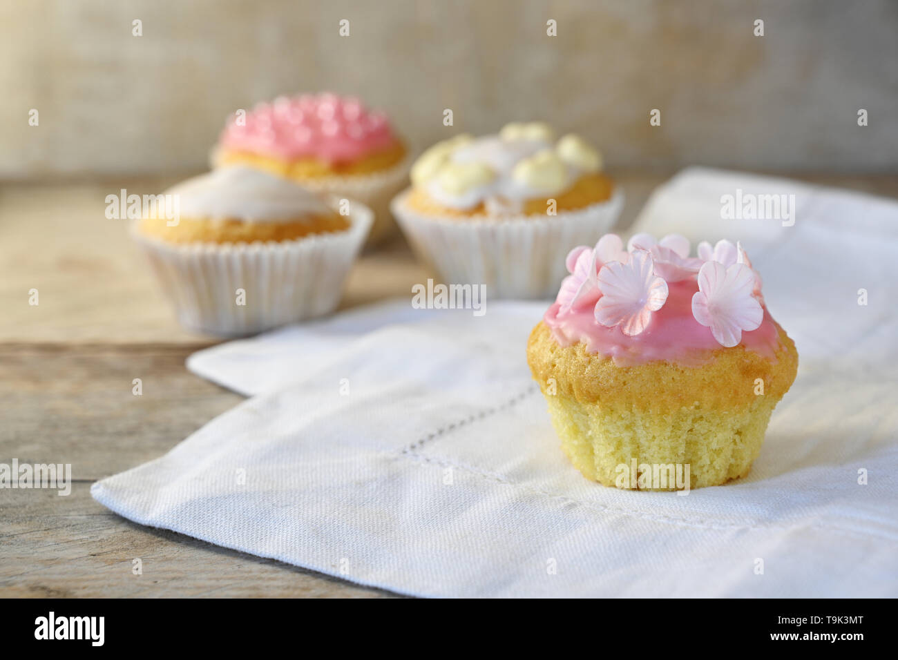 Muffins ou cupcakes avec glaçage rose et d'une décoration florale sur une serviette blanche et une planche en bois rustique, de copie, de l'espace étroit, de discussion, de profondeur fie Banque D'Images