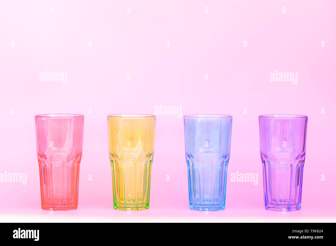 Quatre verres verre identique : rouge, vert, bleu, violet. Quatre tasses en verre multicolore de boissons sur un fond rose. Close-up Banque D'Images