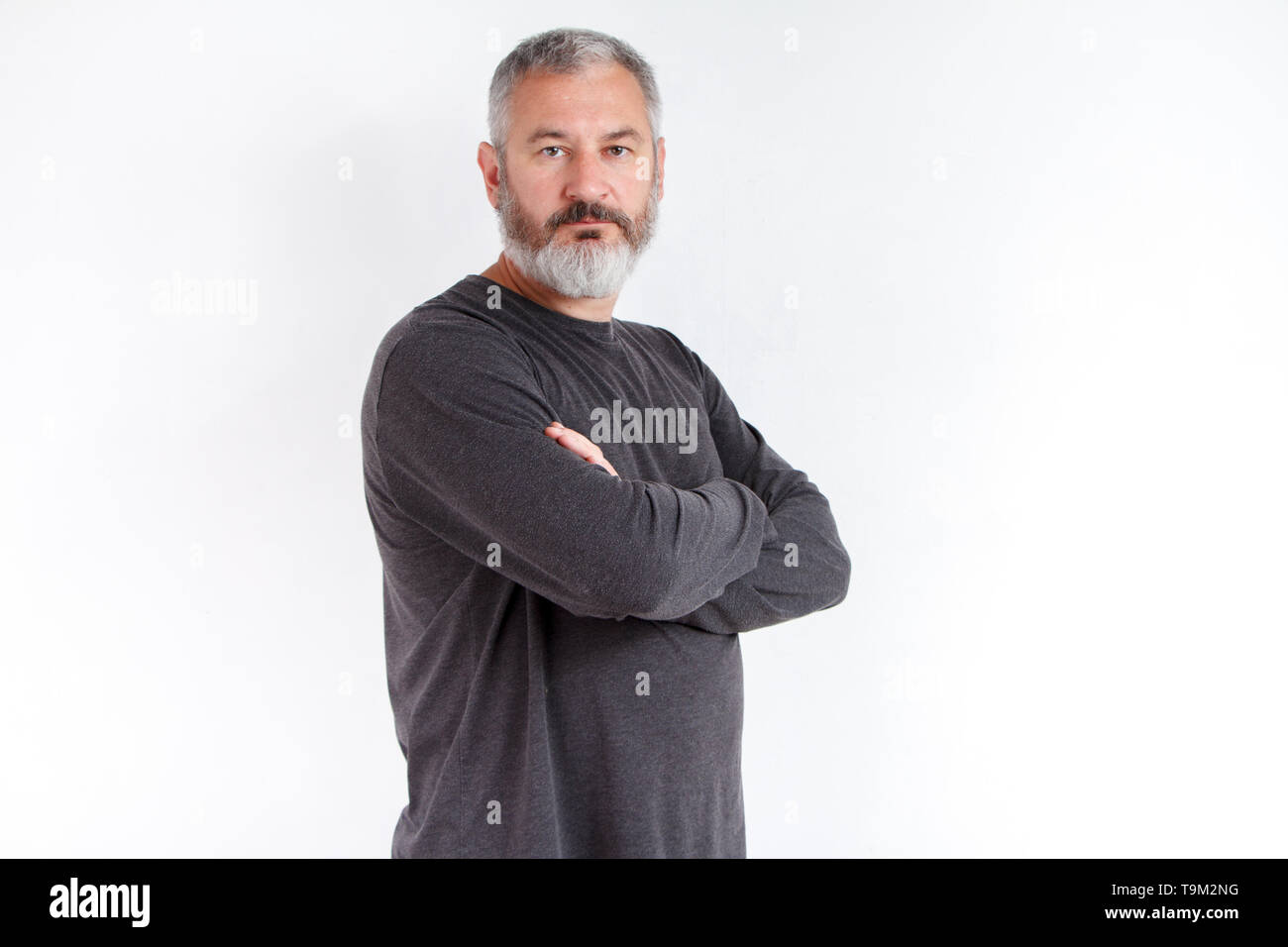 Portrait de mi-longueur d'un homme barbu aux cheveux gris dans un t-shirt gris sur fond blanc. Banque D'Images