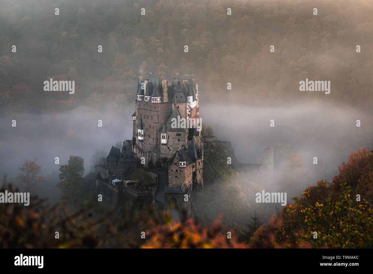 / Burg Eltz Château Eltz pendant le coucher du soleil sur un jour d'automne brumeux d'orangers et de feuilles et le brouillard roulant à travers la vallée (Wierschem, Allemagne) Banque D'Images